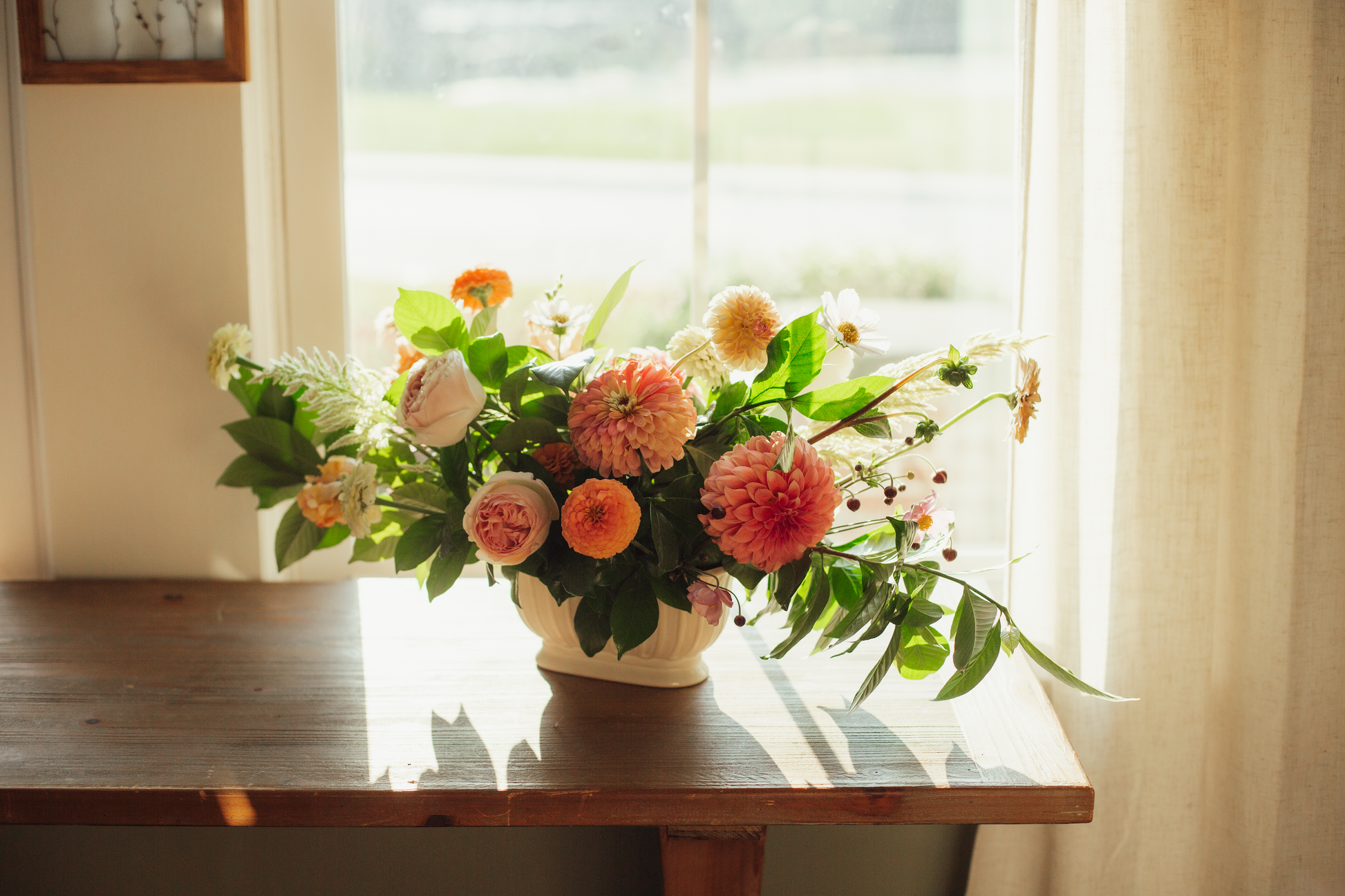 Floral arrangement in a vase on a wooden table with a window in the background