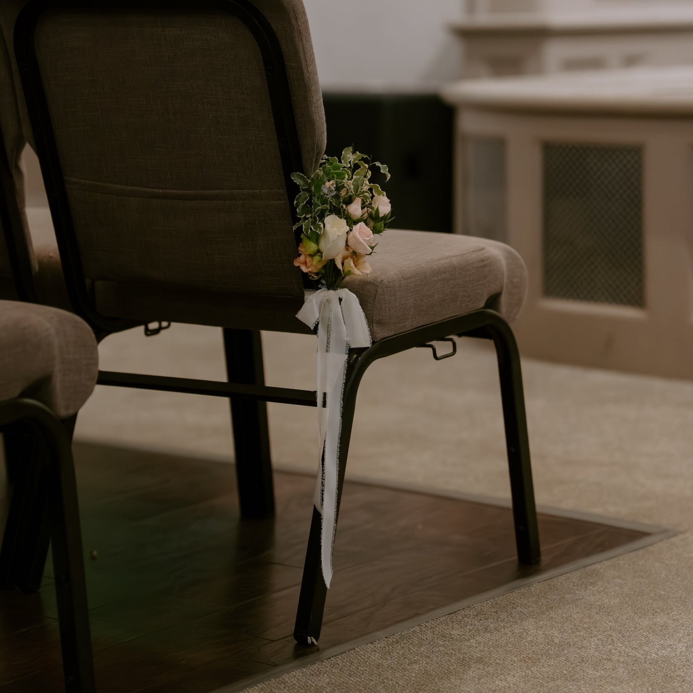 A row of church pews in a church interior, with a small floral arrangement and white ribbon tied to the back of the central pew.