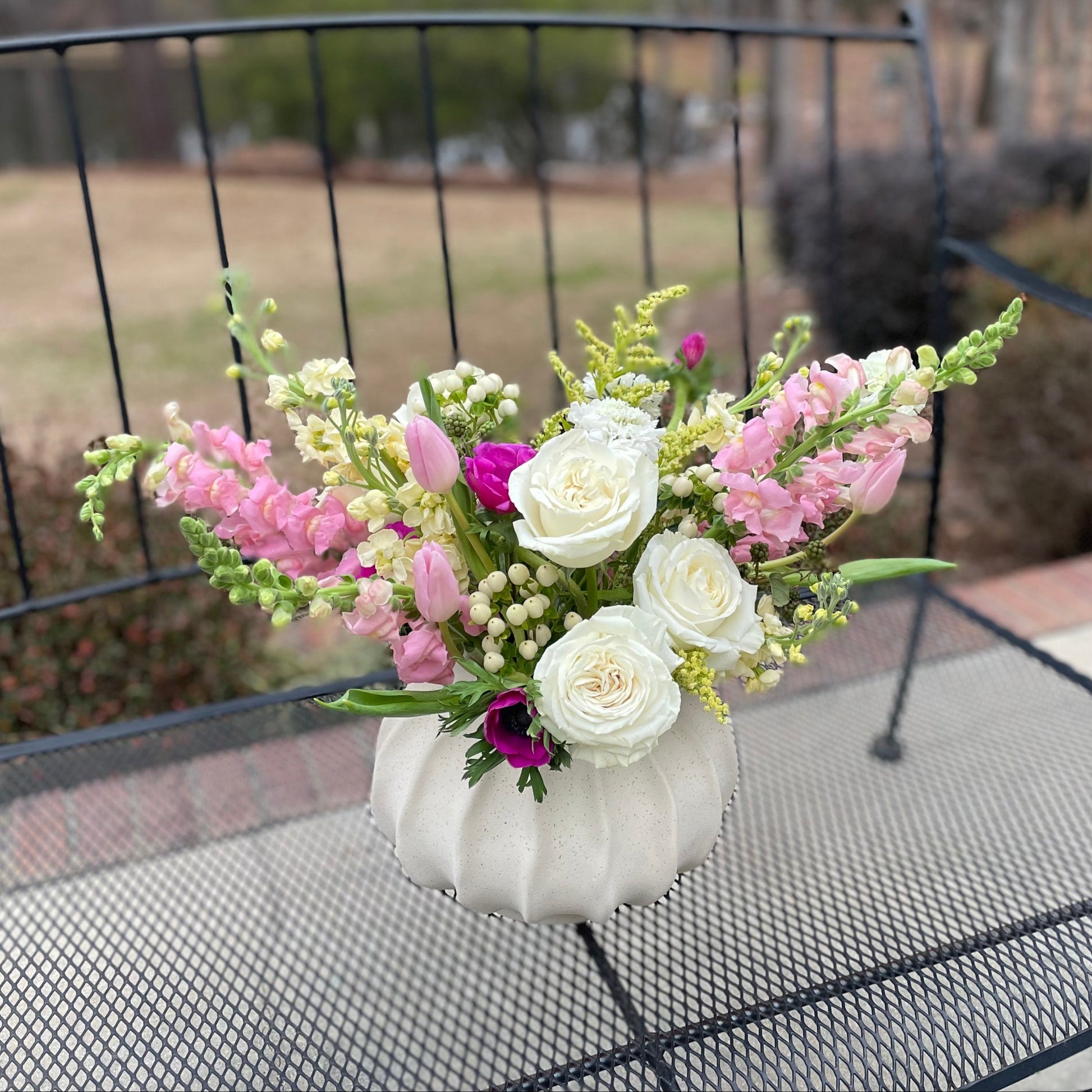 Floral arrangement in a white vase on a metal table outdoors.
