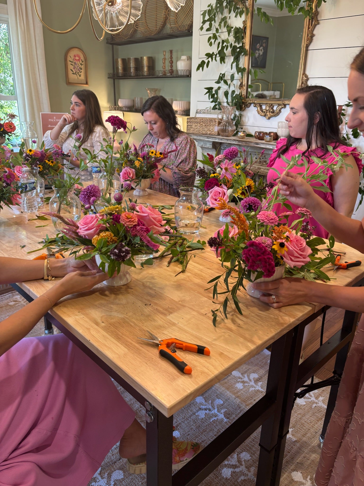 Group of women at a table making floral arrangements in a home setting.