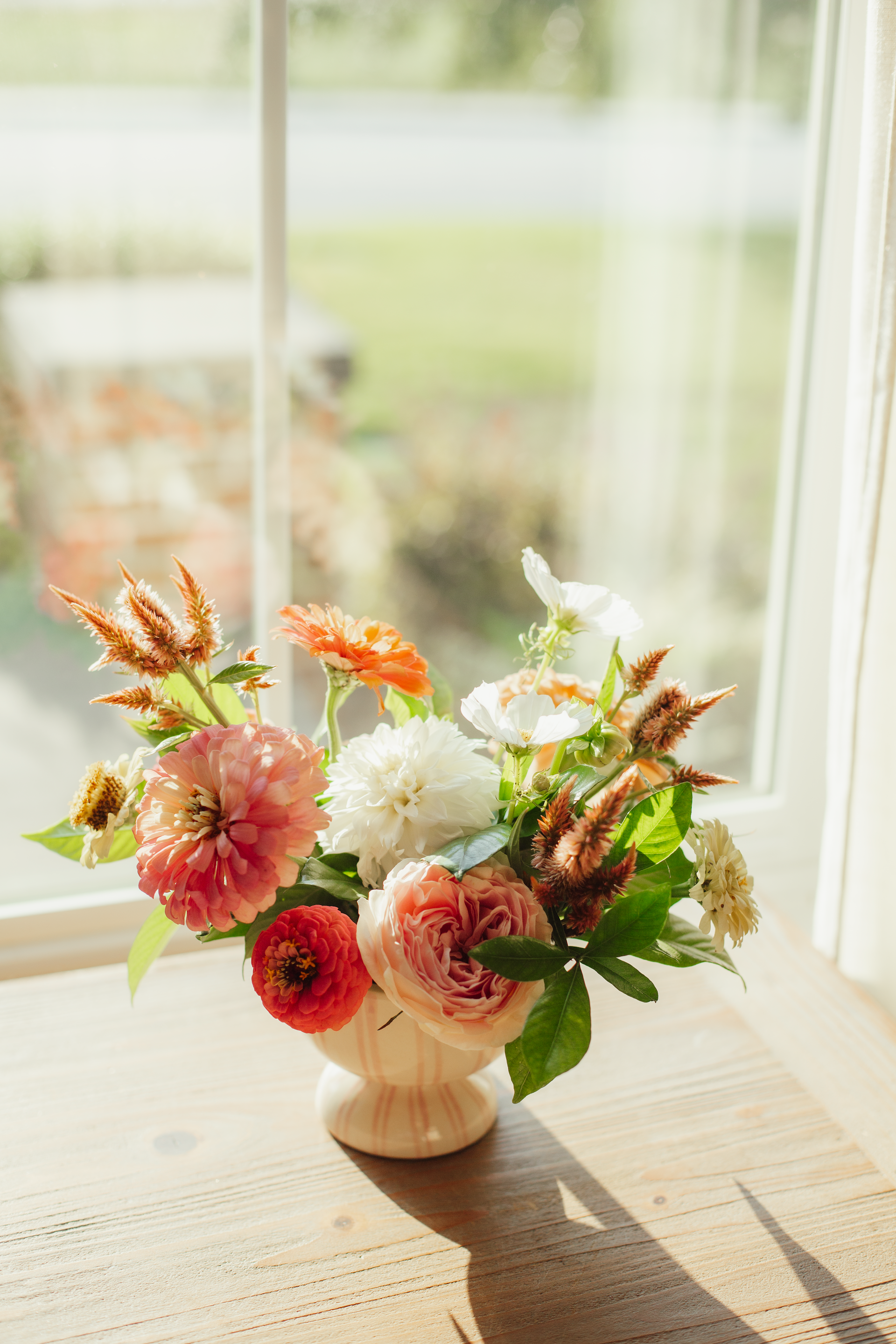 Floral arrangement in a white vase on a wooden surface with a blurred background