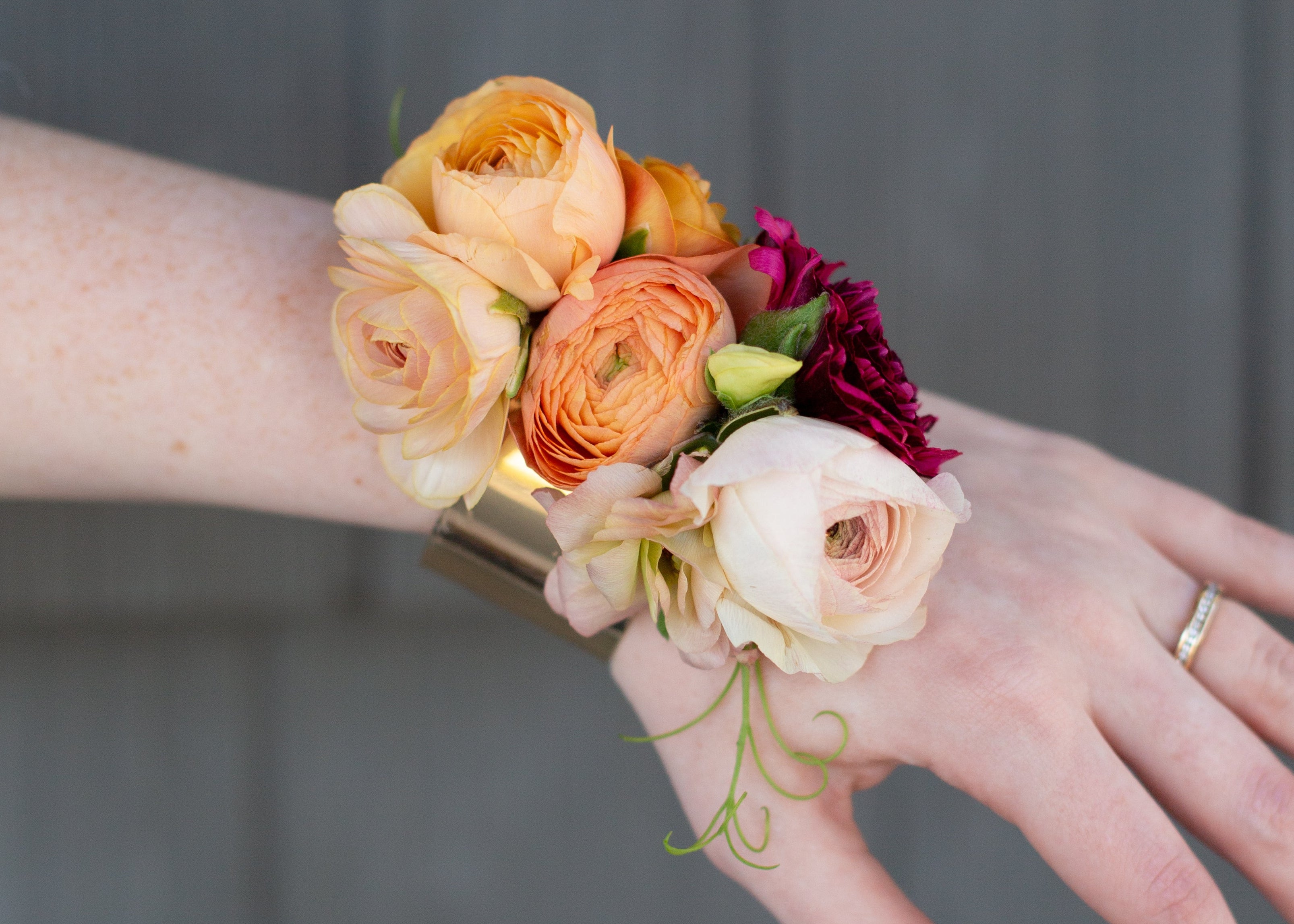 Hand wearing a floral wrist corsage against a gray background